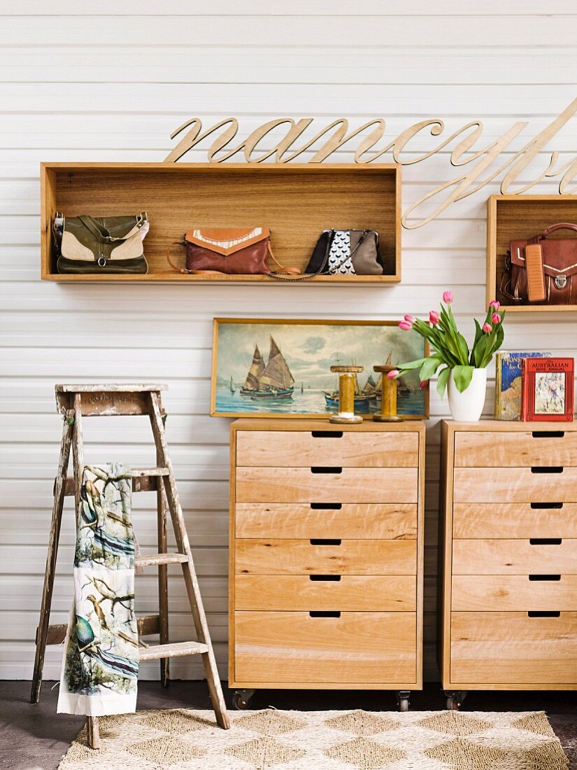Vintage-style hall decor - lettering above handbags in wall-mounted shelving units; old, painter's stepladder and still-life arrangement on wooden chests of drawers