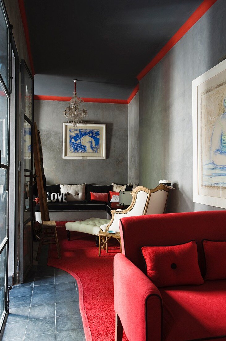Rot und weiss bezogene Polstermöbel in grauem Raum mit moderner Kunst an den Wänden; den Übergang zur Decke ziert ein roter Streifen