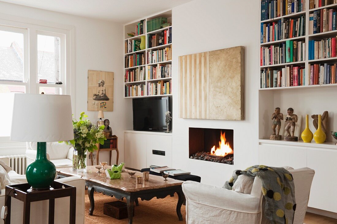 Moderne Malerei über Kamin offene Bücherregale, Couchtisch mit Marmorplatte und weiße Sessel im Wohnzimmer