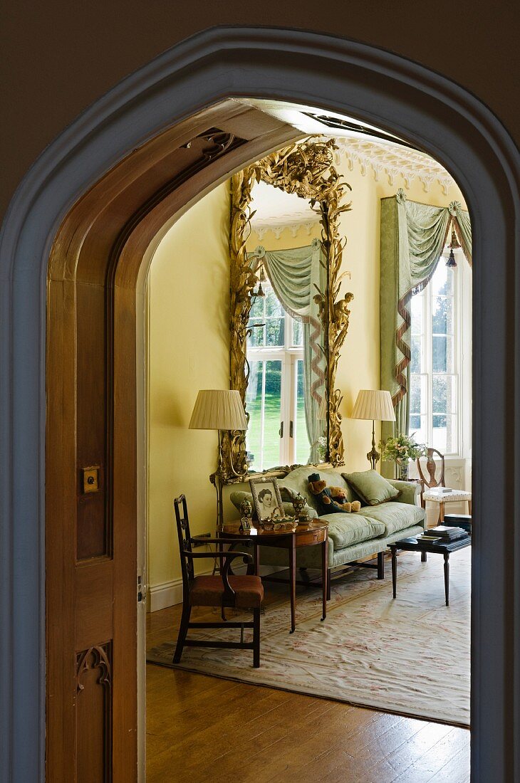 View into grand living area with Baroque wall-mounted mirror, upholstered sofa and standard lamps