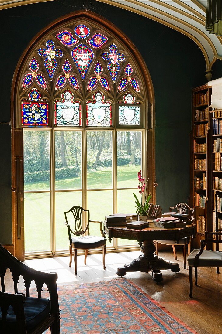 Bibliotheksausschnitt eines englischen Anwesens mit Blick durch das sakrale große Fenster in die sommerliche Parkanlage