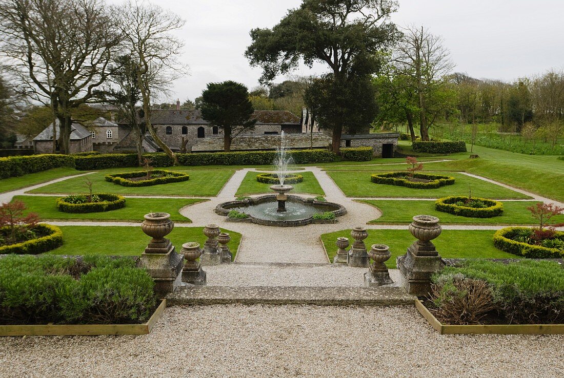 Englische Gartenanlage mit zentralem Brunnen und traditionellem Anwesen im Hintergrund