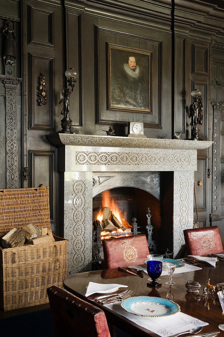 Brennendes Kaminfeuer in dunkelvertäfeltem Speisezimmer eines englischen Anwesens mit festllich gedecktem Tisch