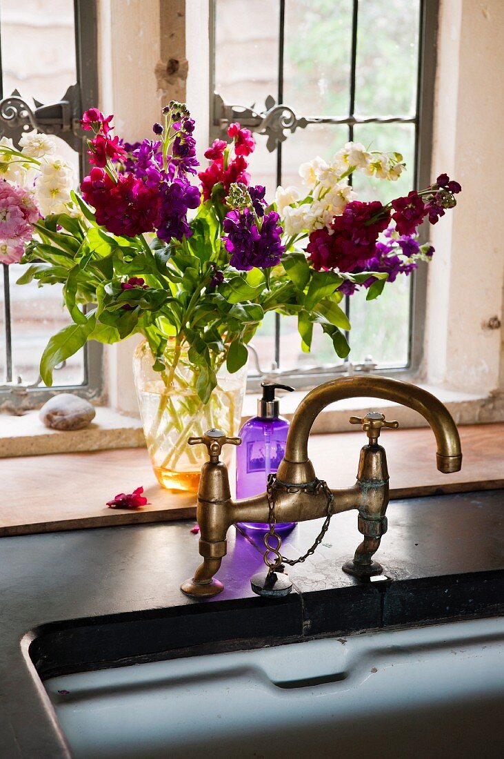 Nostalgische Waschbeckenarmatur auf Steinplatte über Porzellanbecken, sommerlicher Blumenstrauß steht vor dem Fenster