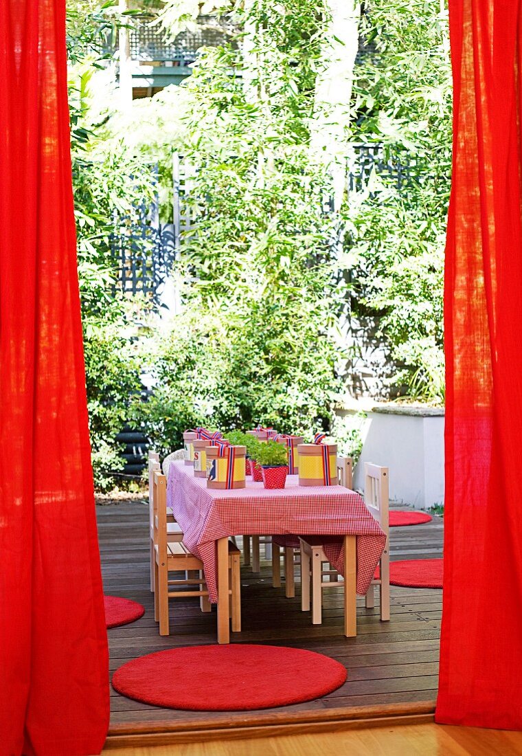 Roter Vorhang auf für die Kinderparty - dekorierter Tisch mit kleinen Stühlen aus Holz auf Terrasse