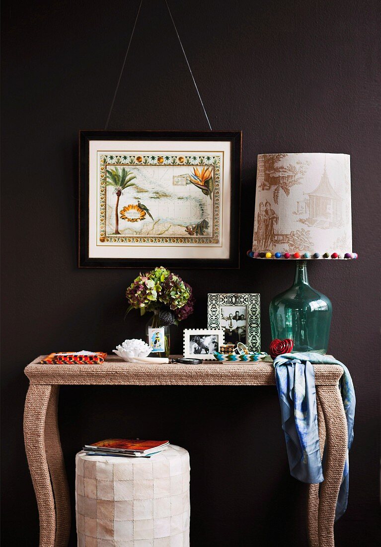 Homemade table lamps on a wall console with curved legs in front of a black wall with a picture hanging on it