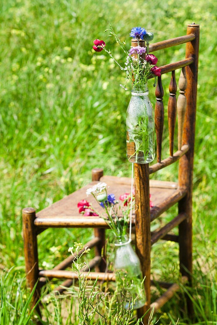 Bottles with wild flowers hanging on a wooden chair