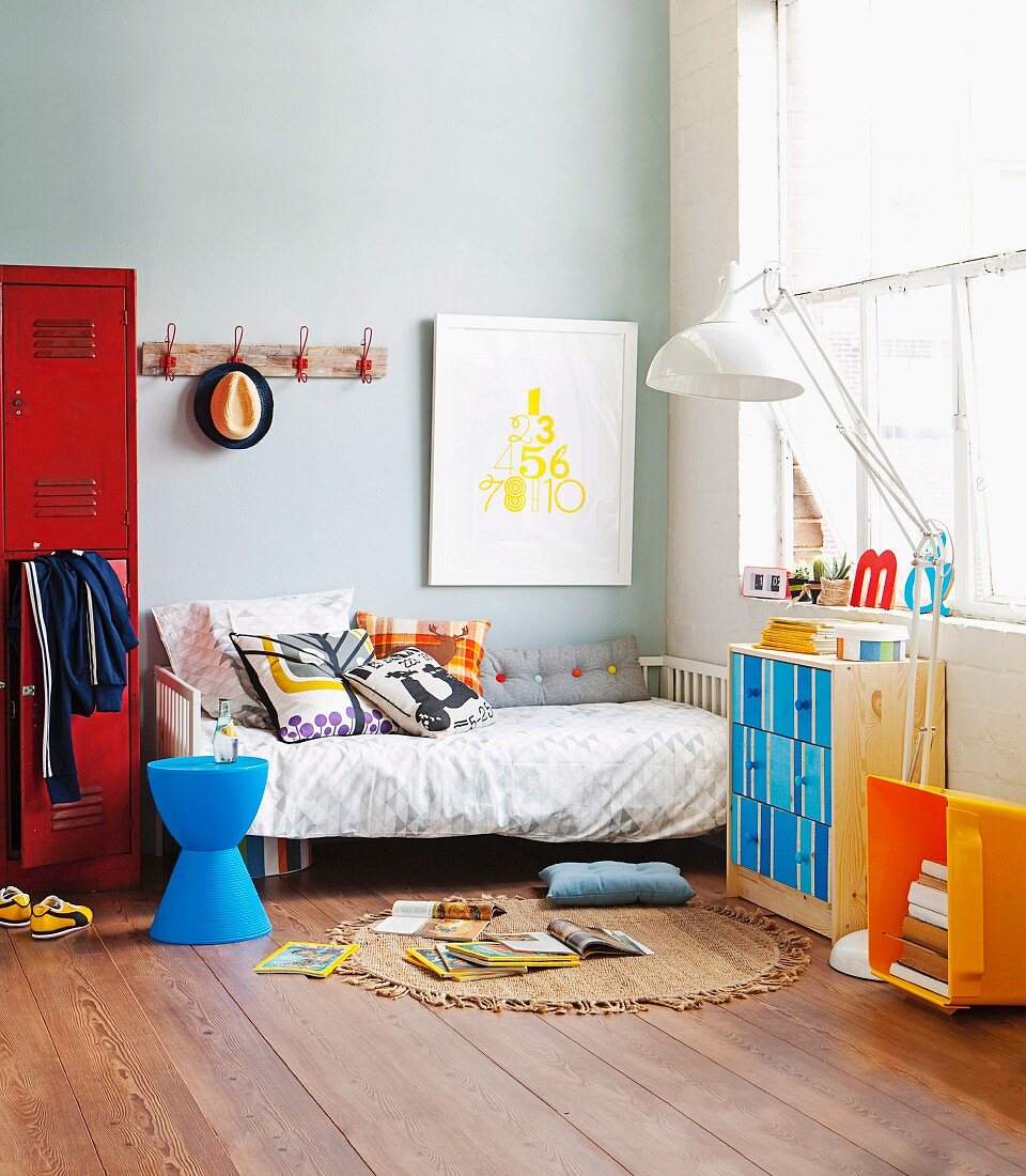 Jungenzimmer mit Bett, rotem Spind und Kommode mit bunten Schubladen