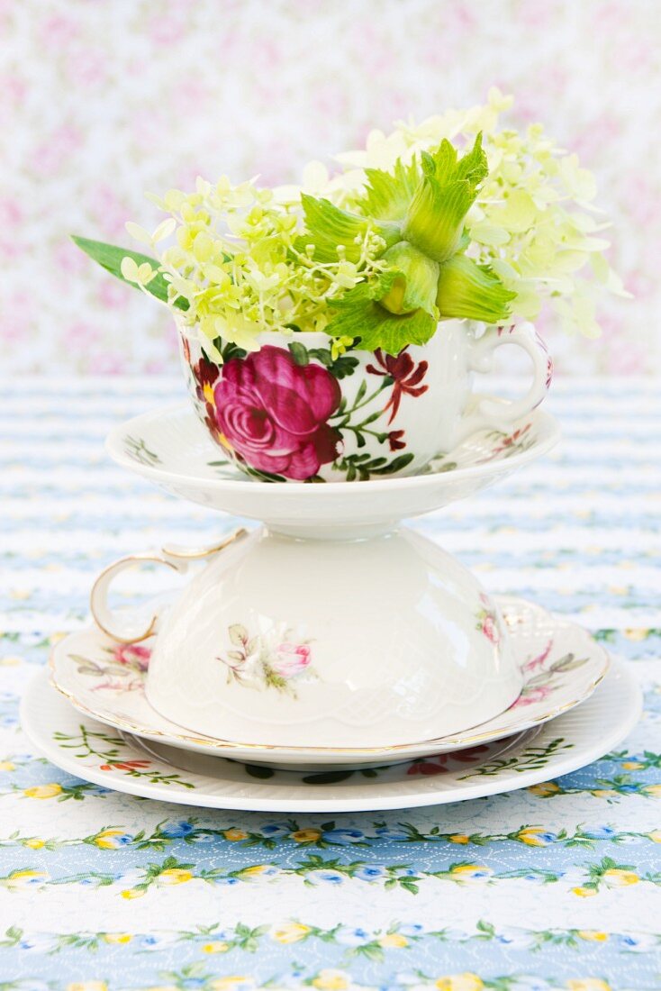 Hydrangea flowers and green hazel nuts in a tower made from an ornamental cup, saucer and plate