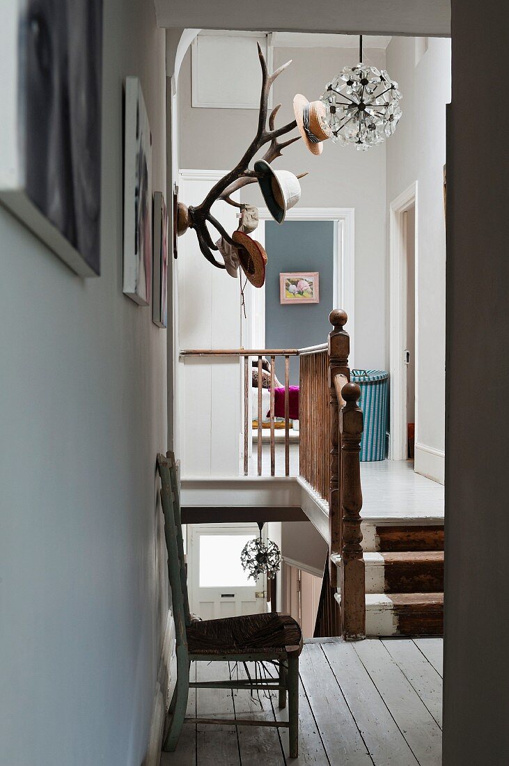 Verwinkeltes Treppenhaus mit weissen Dielen und Holzgeländer; ein Hirschgeweih dient als Garderobe