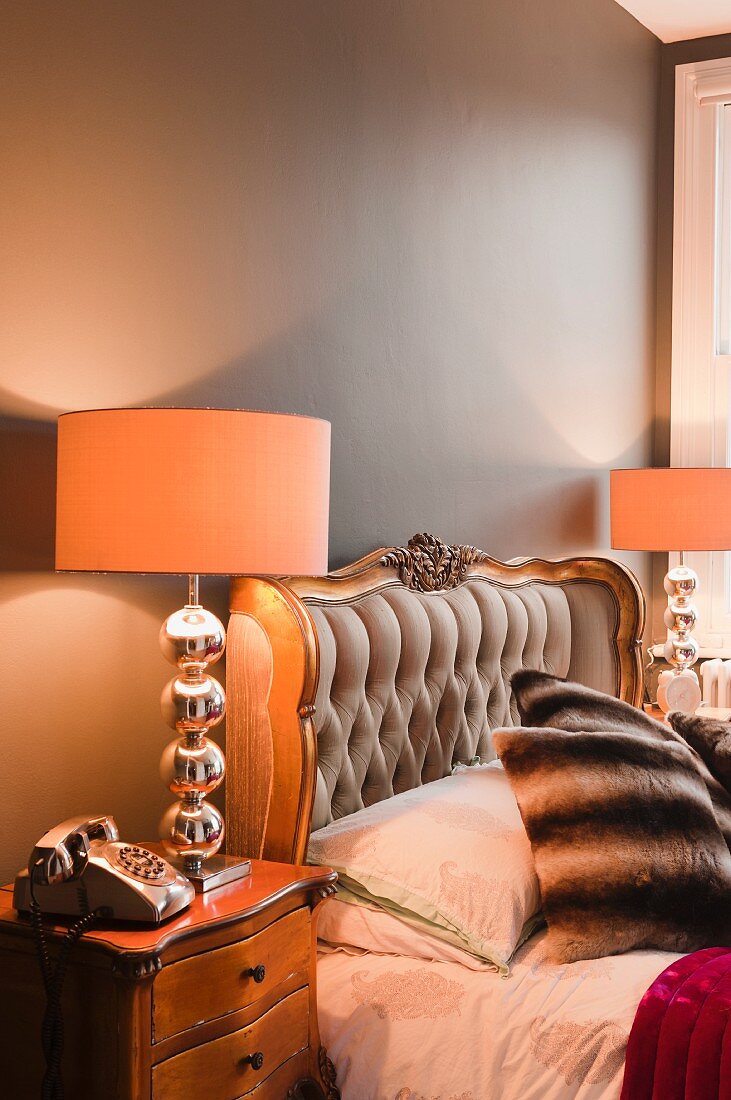 Prunkvolles Bett mit gestepptem Kopfende und vergoldetem Rahmen; auf jeder Seite eine Nachttischlampe mit silberglänzendem Lampenfuss