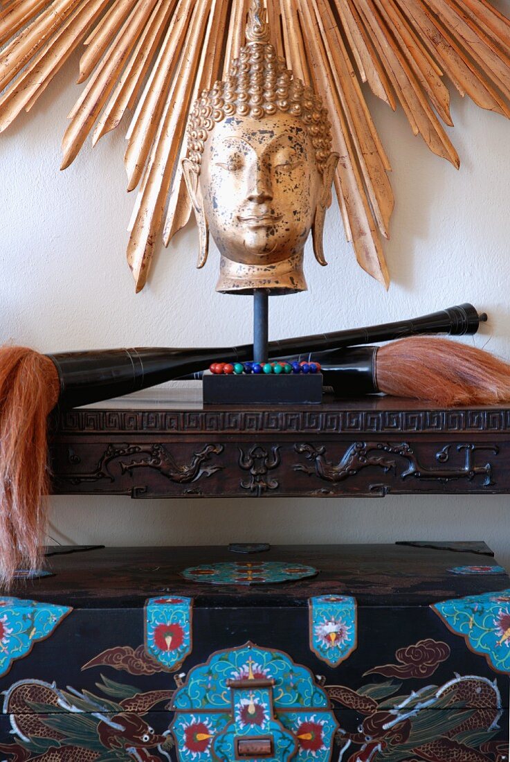 Buddha-Kopf auf geschnitztem Wandtisch vor Wand mit strahlenförmigem Rahmen