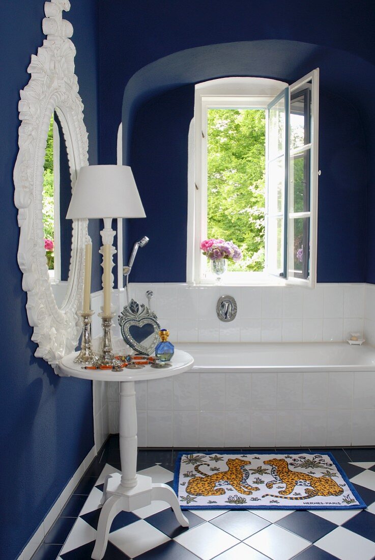 Traditionelles Bad in Weiß-Blau - Weissgeflieste Badewanne vor offenem Fenster mit Gartenblick in dunkelblau getöntem Bad