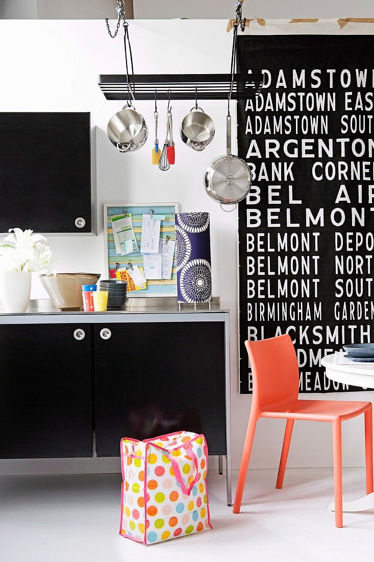 Jugendlich freche Kücheneinrichtung mit grossem schwarz-weißem Schriftbild, aufgehängten Töpfen und knalligem orangem Kunststoffstuhl