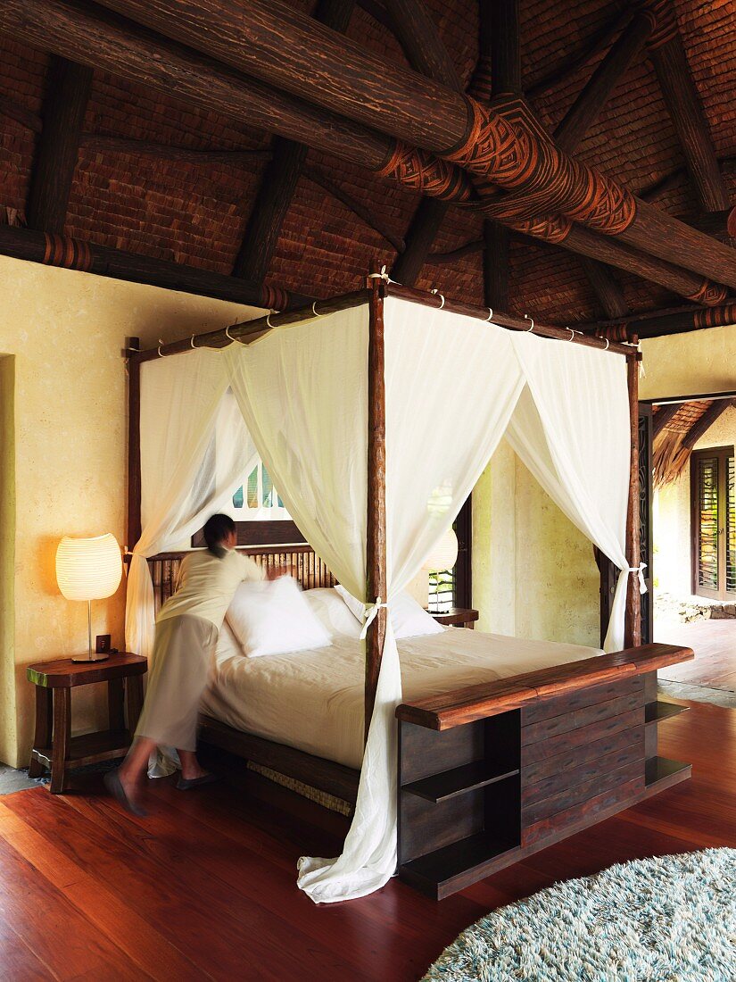 Zimmermädchen richtet das Bett in elegantem, asiatischem Holzhaus