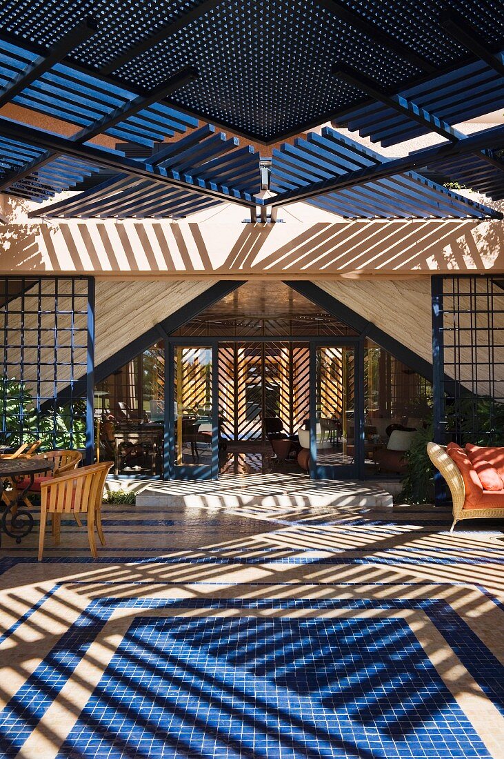 A painted wood screen provides shade over a garden terrace with tiled flooring