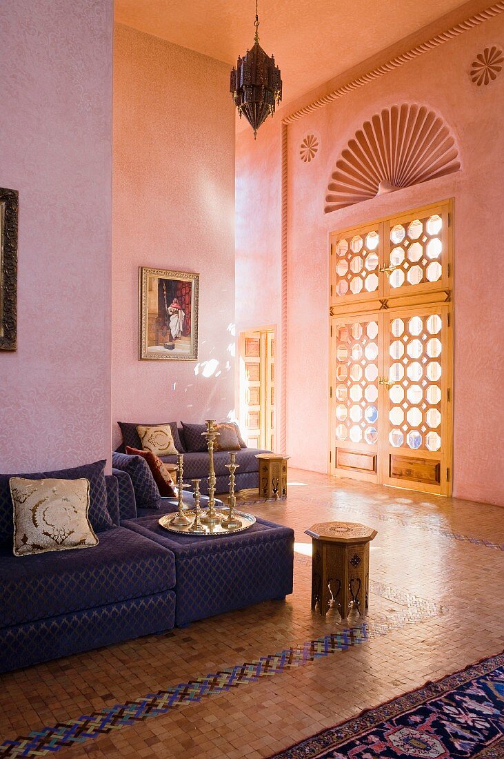 Tablett mit Kerzenständern auf gepolsterter Sitzbank vor rosa getönter Wand und Flügeltür mit kreisförmigen Ausschnitten in Holztür