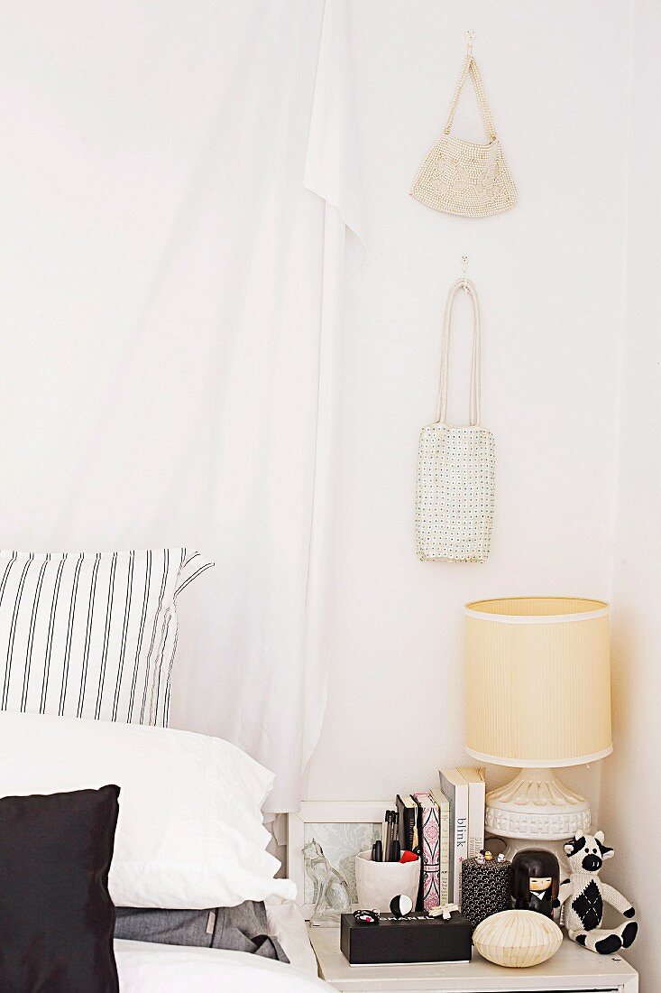 Drappierter Vorhang am Bettkopf und Handtaschen an der Wand über dem Nachttisch in einem Schlafzimmer