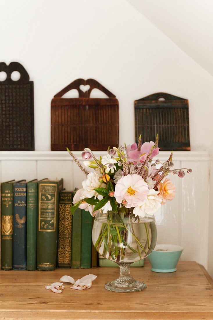 Prachtvoller Sommerstrauss in einer Glasvase vor antiken Büchern auf einer Holzkommode stehend