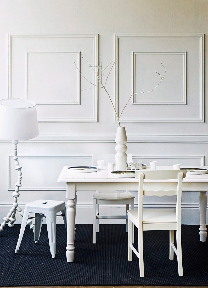 White lacquer dining table with tiled top on a black carpet in front of a white, wood paneled wall