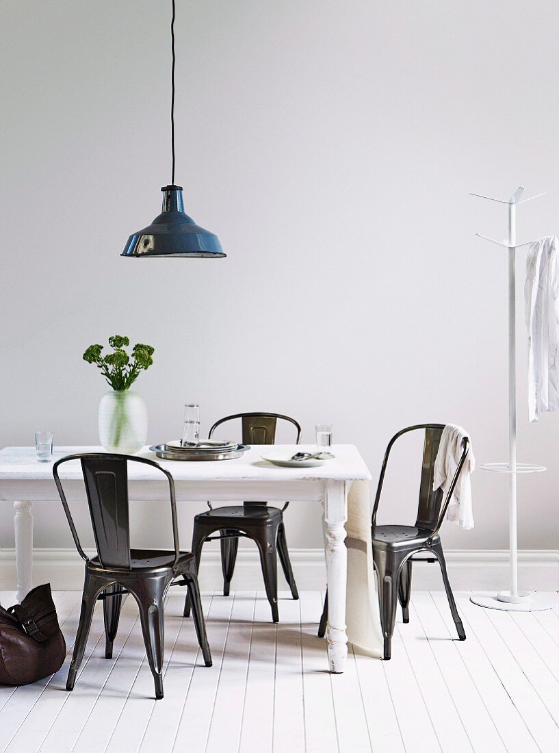 White lacquer, shabby chic dining table with black metal chairs and a black metal hanging lamp above