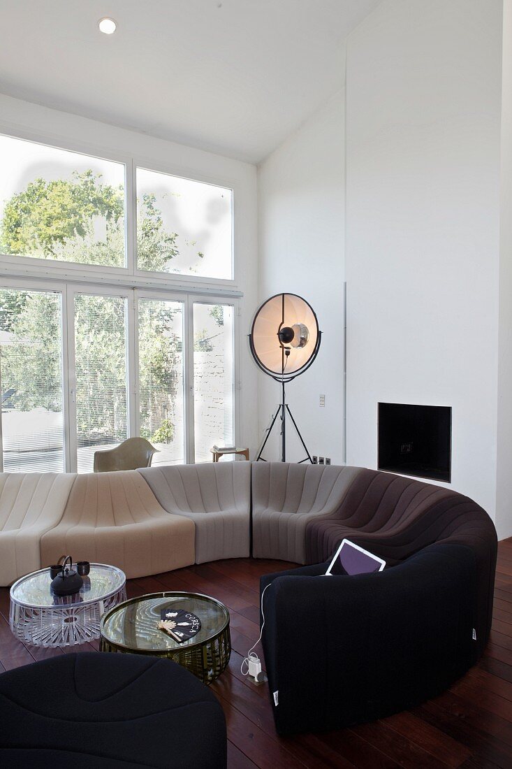 Zeitgenössische Sofakombination vor großer Fensterfont in einem Wohnzimmer mit dunklem Dielenboden und hoher, schräger Decke