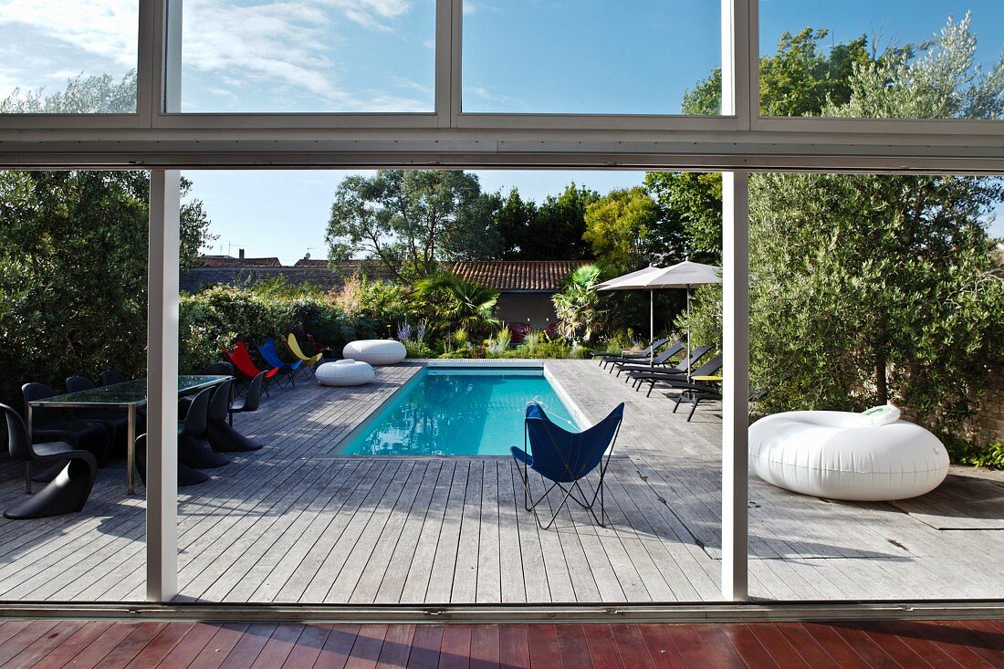 Blick durch die geöffnete Terrassentür auf die große Holzterrasse mit Pool und Designermöbeln