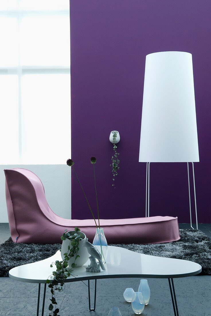 Zeitgenössisches Wohnzimmer mit Couchtisch, Liege und Stehleuchte im Designerstil vor violetter Wand