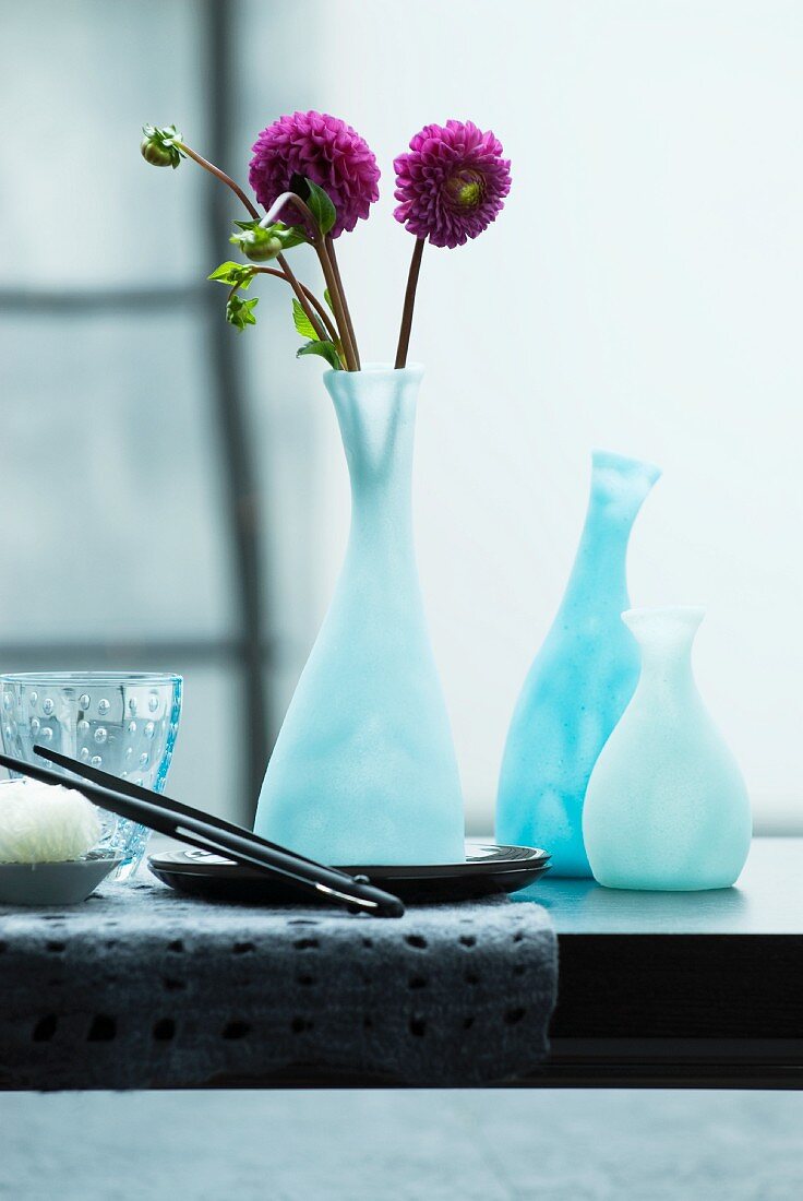 Moderne Blumenvase mit violetten Dahlien auf einem schwarzen Esstisch