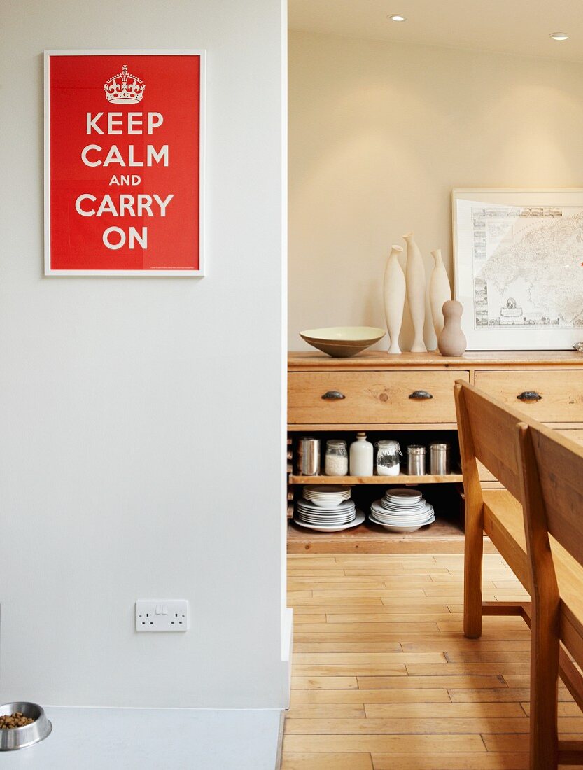 Red and white picture with slogan, sideboard and wooden bench in dining room