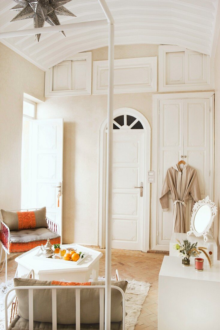 Loungeecke mit gepolsterten Metallstühlen und weißem Beistelltischchen vor Wand mit eingebauten Schrankelementen in orientalischem Schlafzimmer