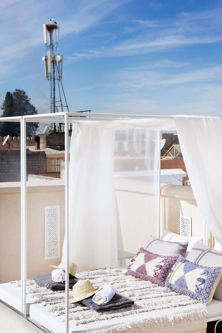 Einladend vorbereitetes modernes Tagesdoppelbett mit luftigem Stoffhimmel auf orientalischer Dachterrasse unter freiem blauem Himmel