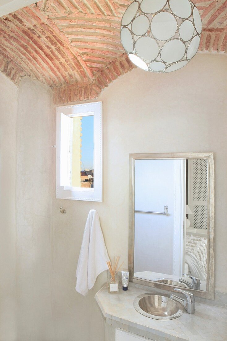 Kugelförmige Pendelleuchte an Gewölbedecke aus Ziegel über schlichtem Waschtisch mit Spiegel in orientalischem Bad; kleiner Ausblick durch das Fenster