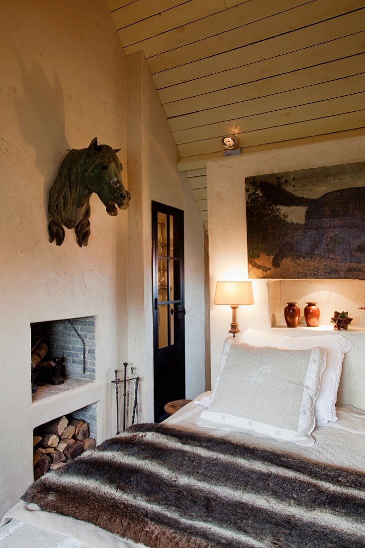 Metal horses head hanging on the wall of a cozy bedroom with a small fireplace a wood panel, pitched ceiling