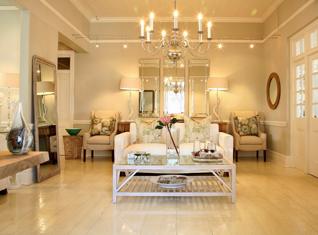 Pale living room with sofa, coffee table, armchairs, mirrors and silver chandelier