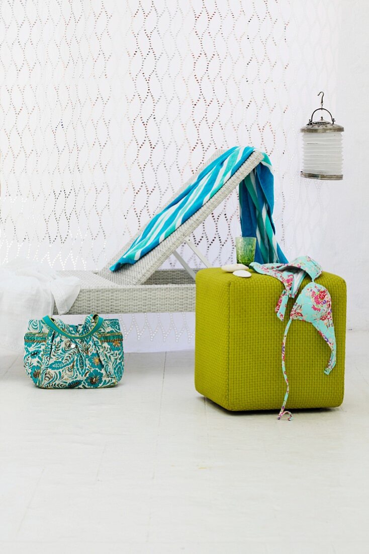 Blue towel on white lounger in front of white curtain; bikini on green, cubic pouffe in foreground