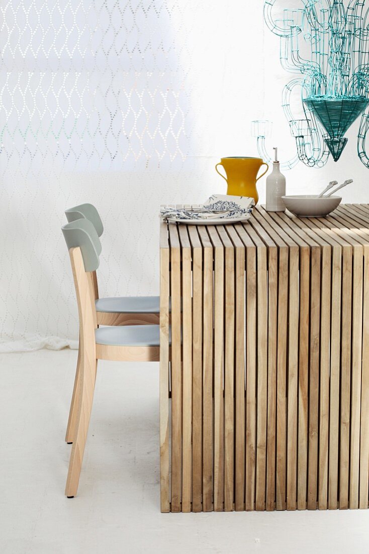 Holztisch aus einzelnen naturbelassenen Holzleisten mit grauen Stühlen vor weißem Vorhang