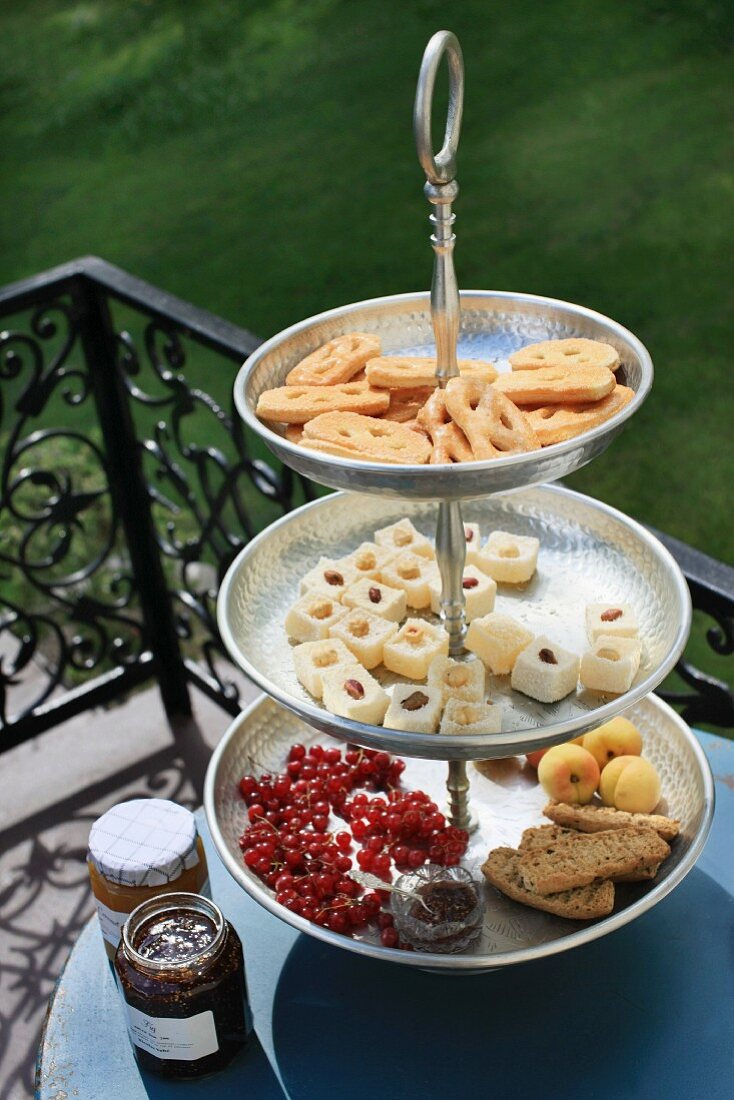 A tiered cake stand with dainty treats on a balcony table, with decorative railings in the background