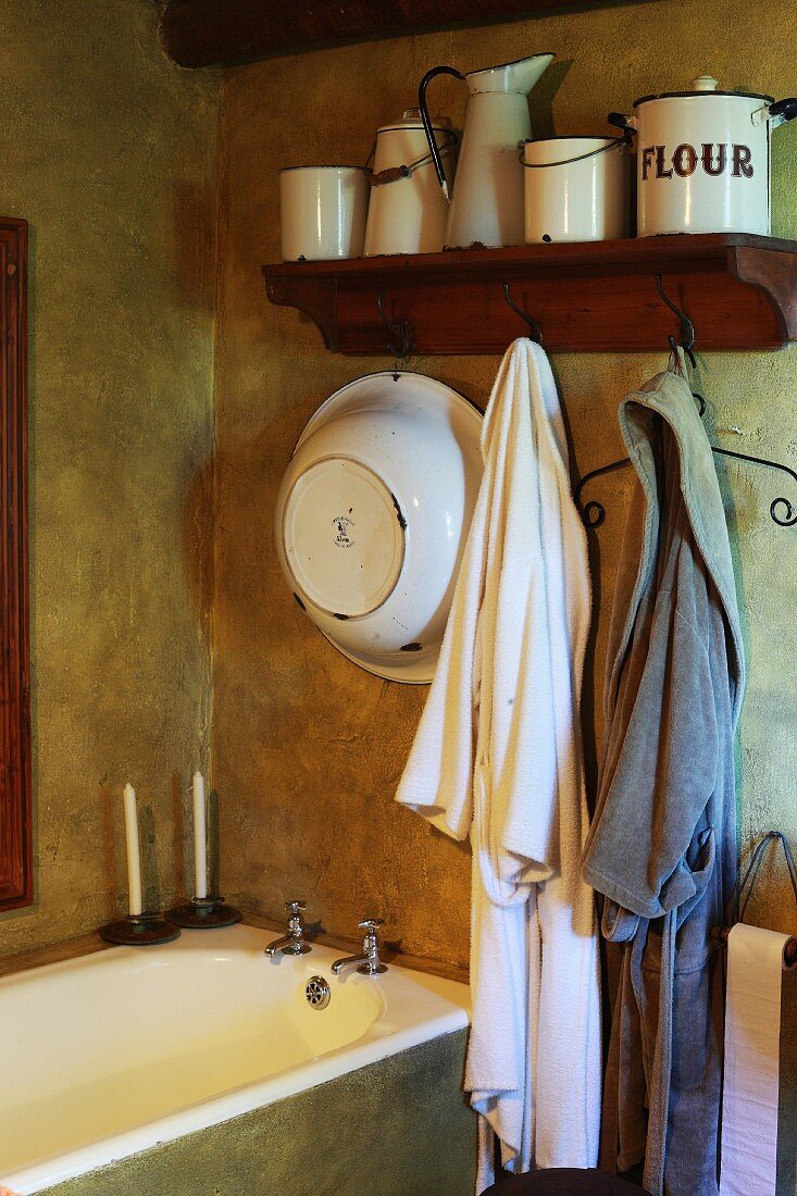 Vintage bathroom in earthy, natural shades with old enamel pots and simple dressing gowns above built-in bathtub