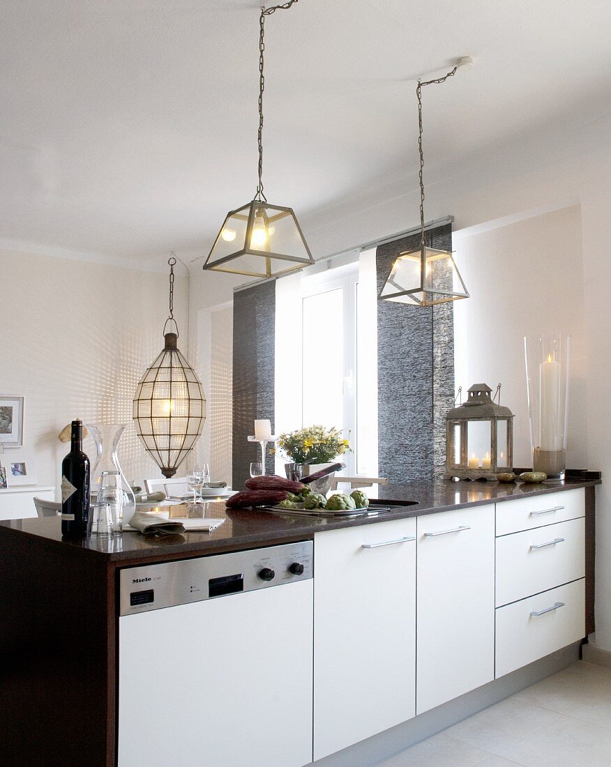 Brightly lit kitchen counter below lamps with glass lampshades; elliptical pendant lamp above dining table