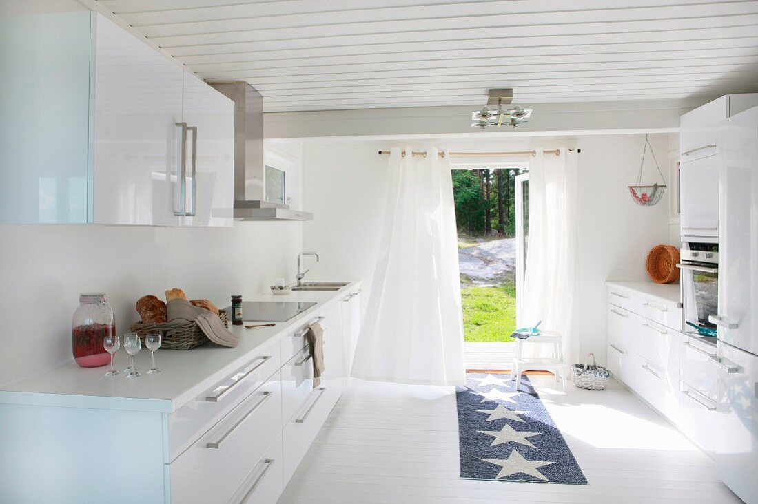 weiße Designerküche mit Teppichläufer vor offener Terrassentür und Blick in Garten