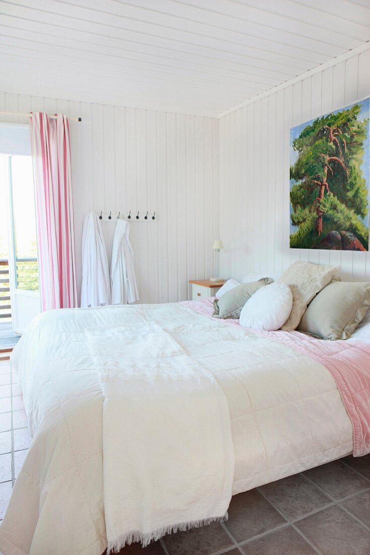 Doppelbett mit weisser Tagesdecke in weißem holzverkleidetem Schlafzimmer