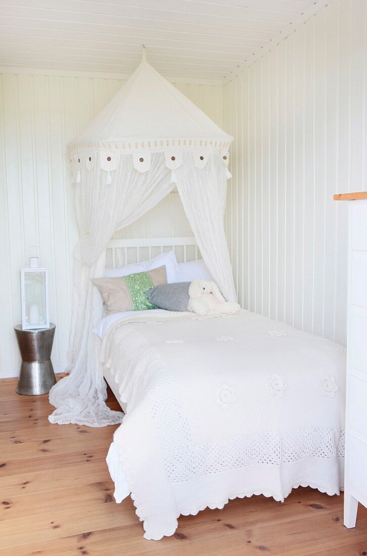 Bed with a canopy and white lace bedspread in a white paneled room