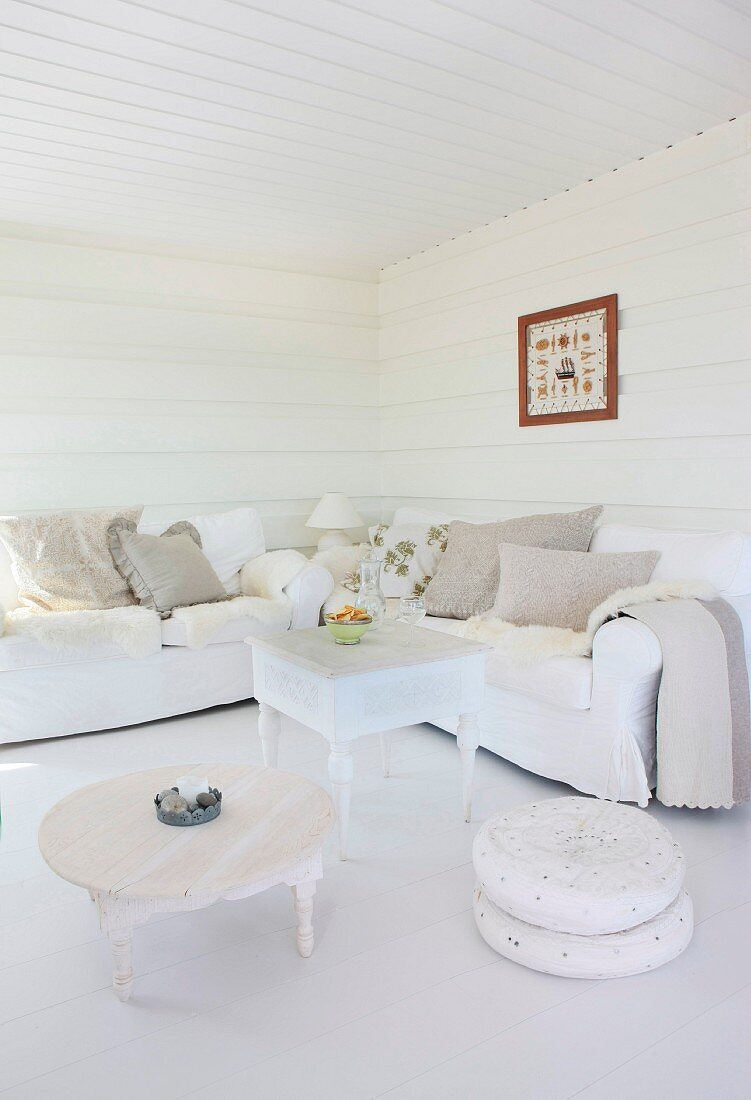 Low coffee table and ottoman next to a coffee table in front of upholstered seating in a white paneled living room