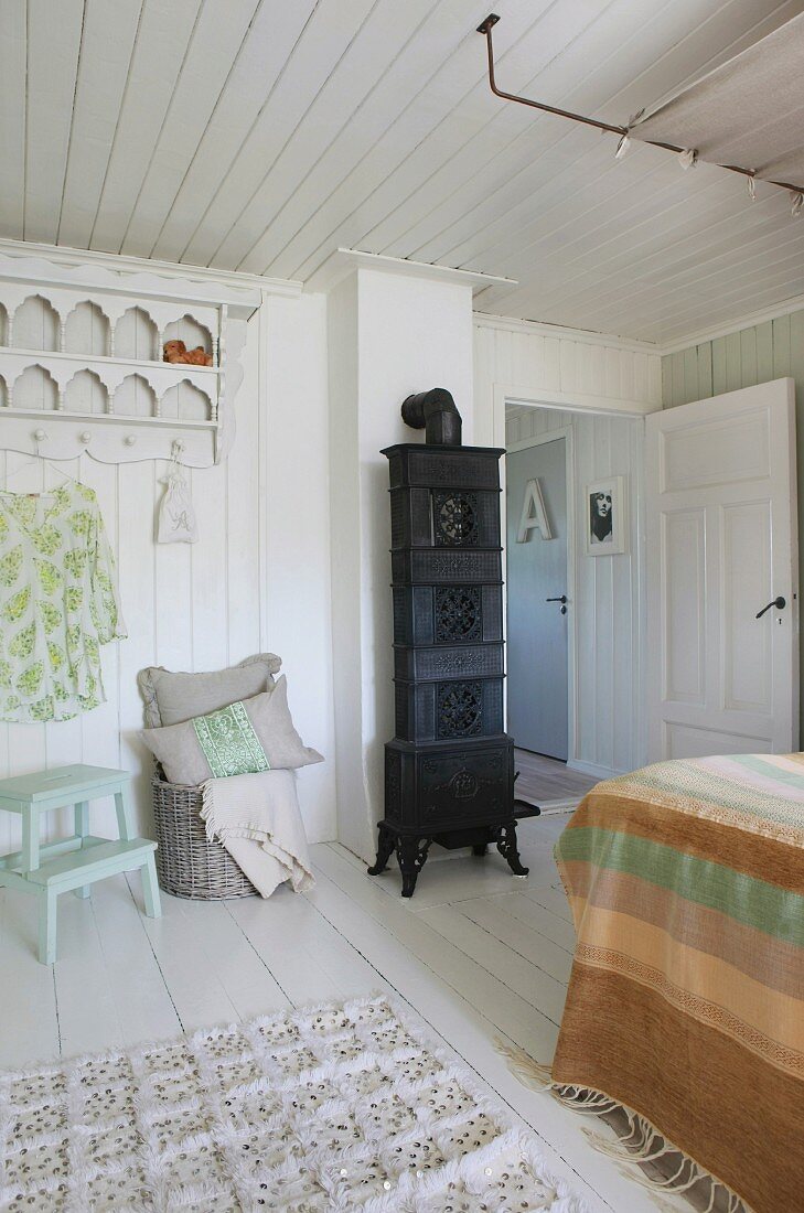 Schwarzer Kaminofen in weißem Holzraum mit verspielter Holzgarderobe und feudalem Bett
