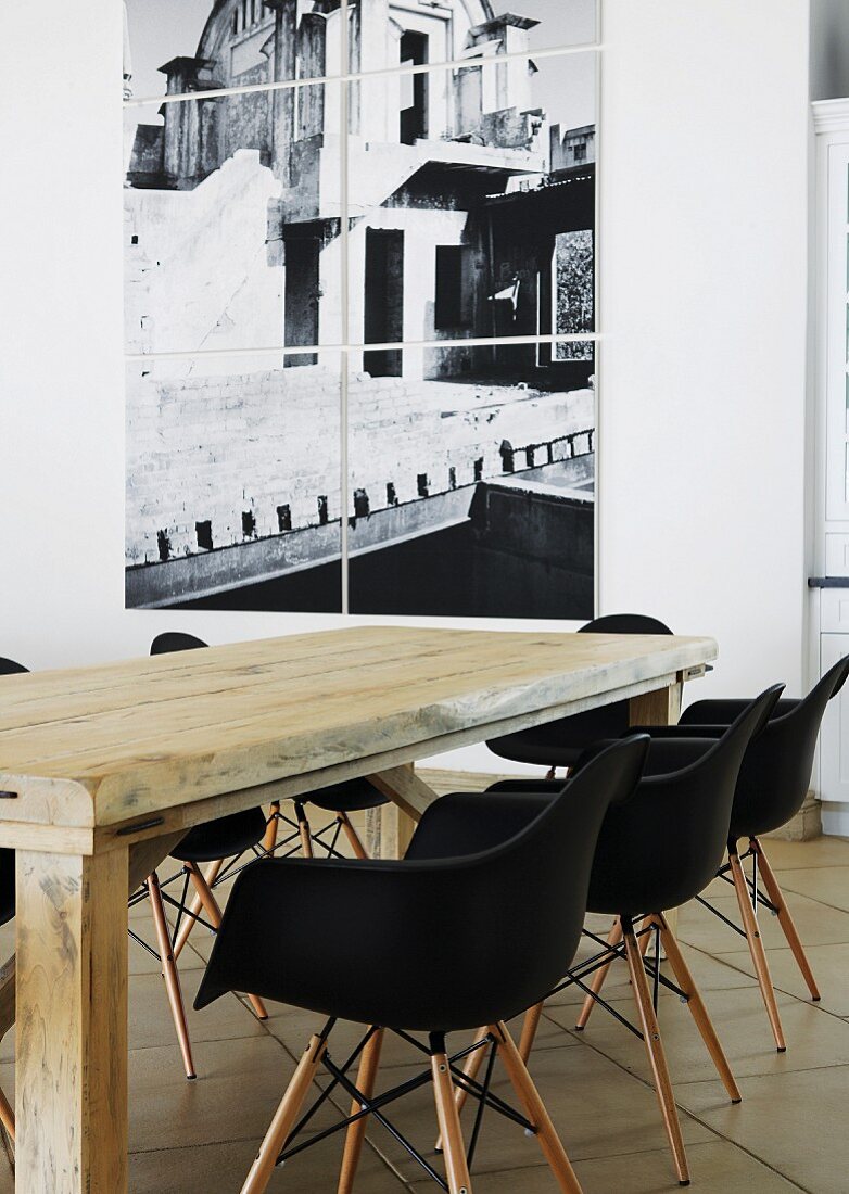 Rustikaler Holztisch mit schwarzen Eames Stühlen vor hängendem Fotobild an weisser Wand