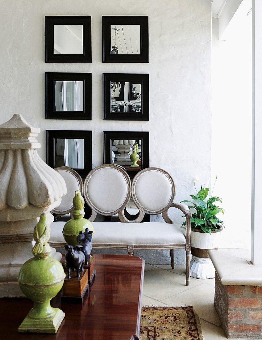 Group of square mirrors with black frames on white wall behind Baroque sofa with white upholstery