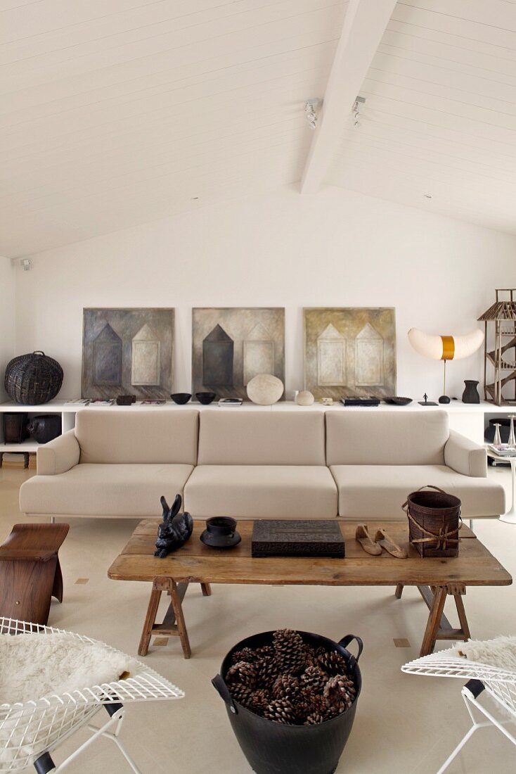 Rustic coffee table in front a designer couch upholstered in light fabric in a modern living room and a row of pictures on the wall