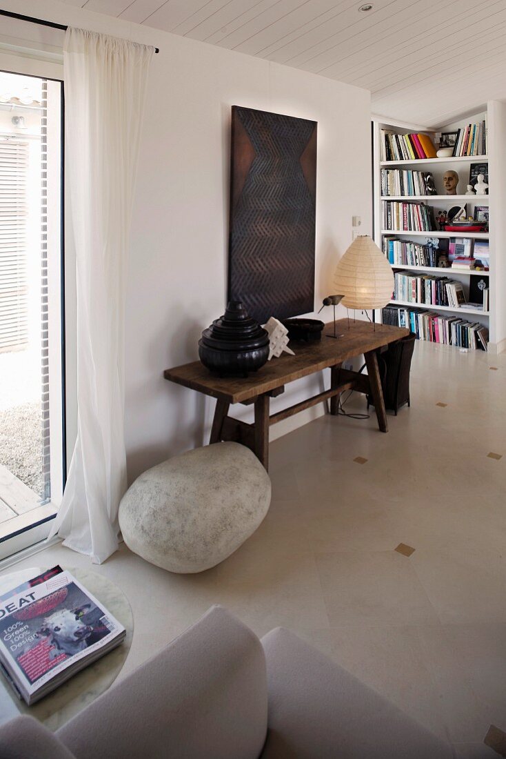 Rustikaler Holztisch an Wand und Steinfindling auf Boden in schlichtem Wohnzimmer