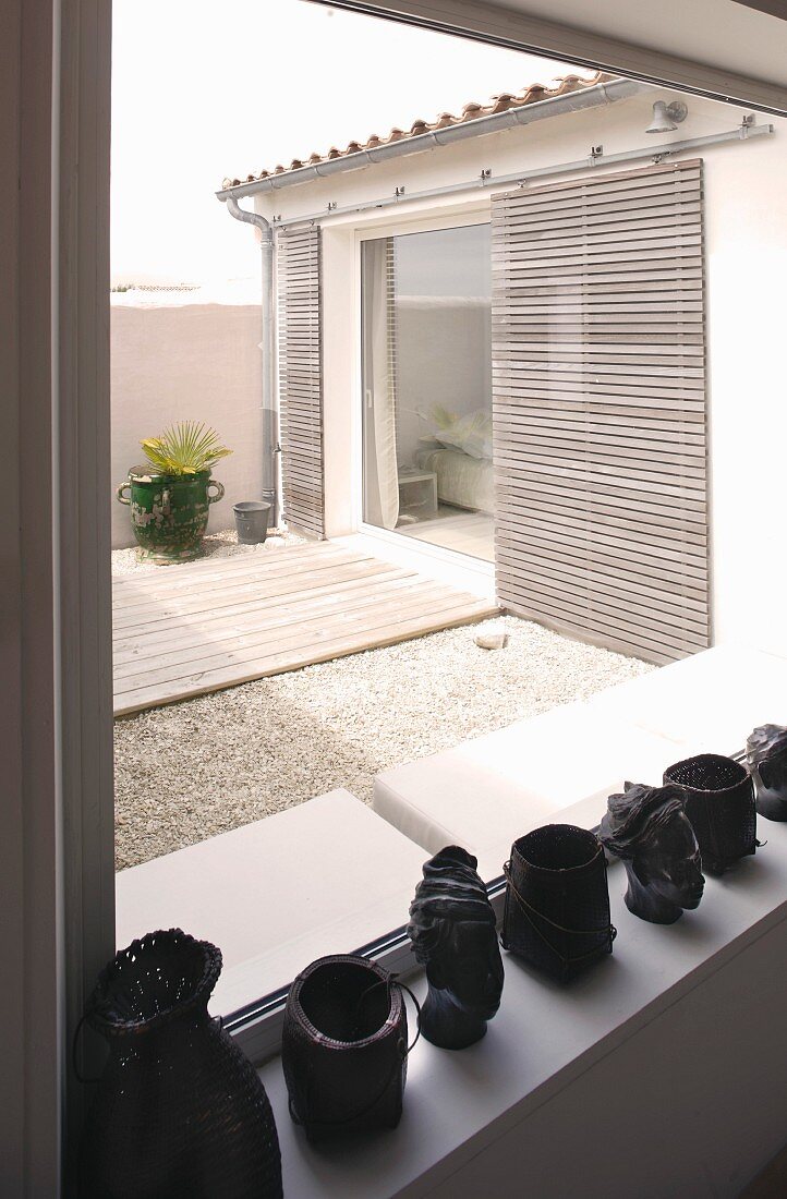 Köpfe und Behälter aus schwarzem Material auf Fensterbank und Blick in Innenhof auf Schiebelemente an Wohnhausfassade